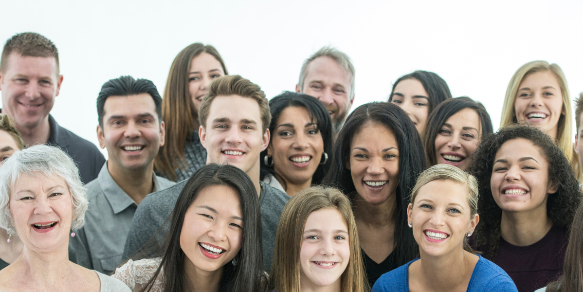 A diverse group of smiling people of different ages, representing multiple generations.