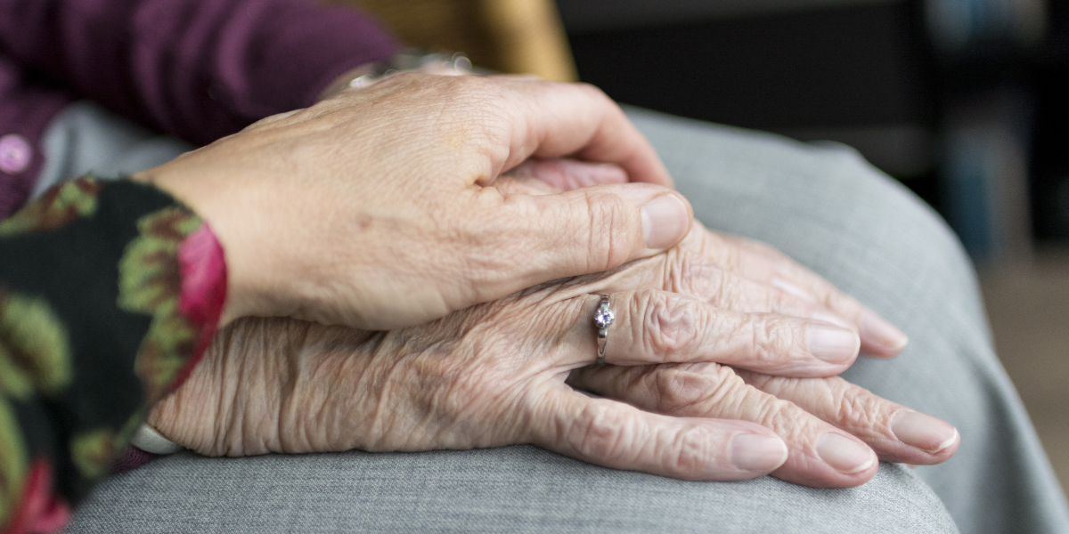 Close-up of two hands, one elderly with a ring on the finger, gently held by a younger hand, symbolizing long-term care and support.