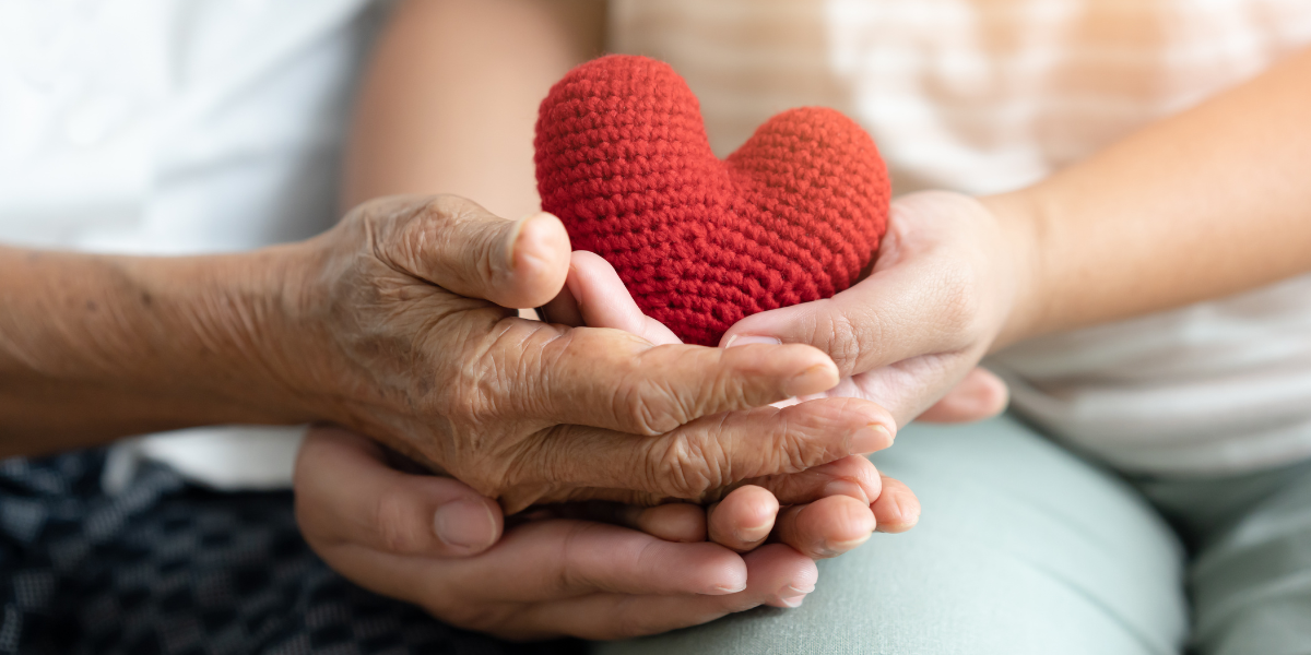Life with LTC - Close-up of elderly and young hands holding a red heart, symbolizing care, compassion, and long-term support